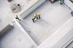 Arial view of construction workers on a roof top with clipboards, talking.